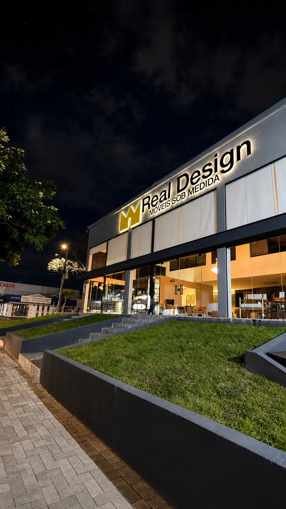 Fachada iluminada da loja Real Design Móveis sob Medida à noite