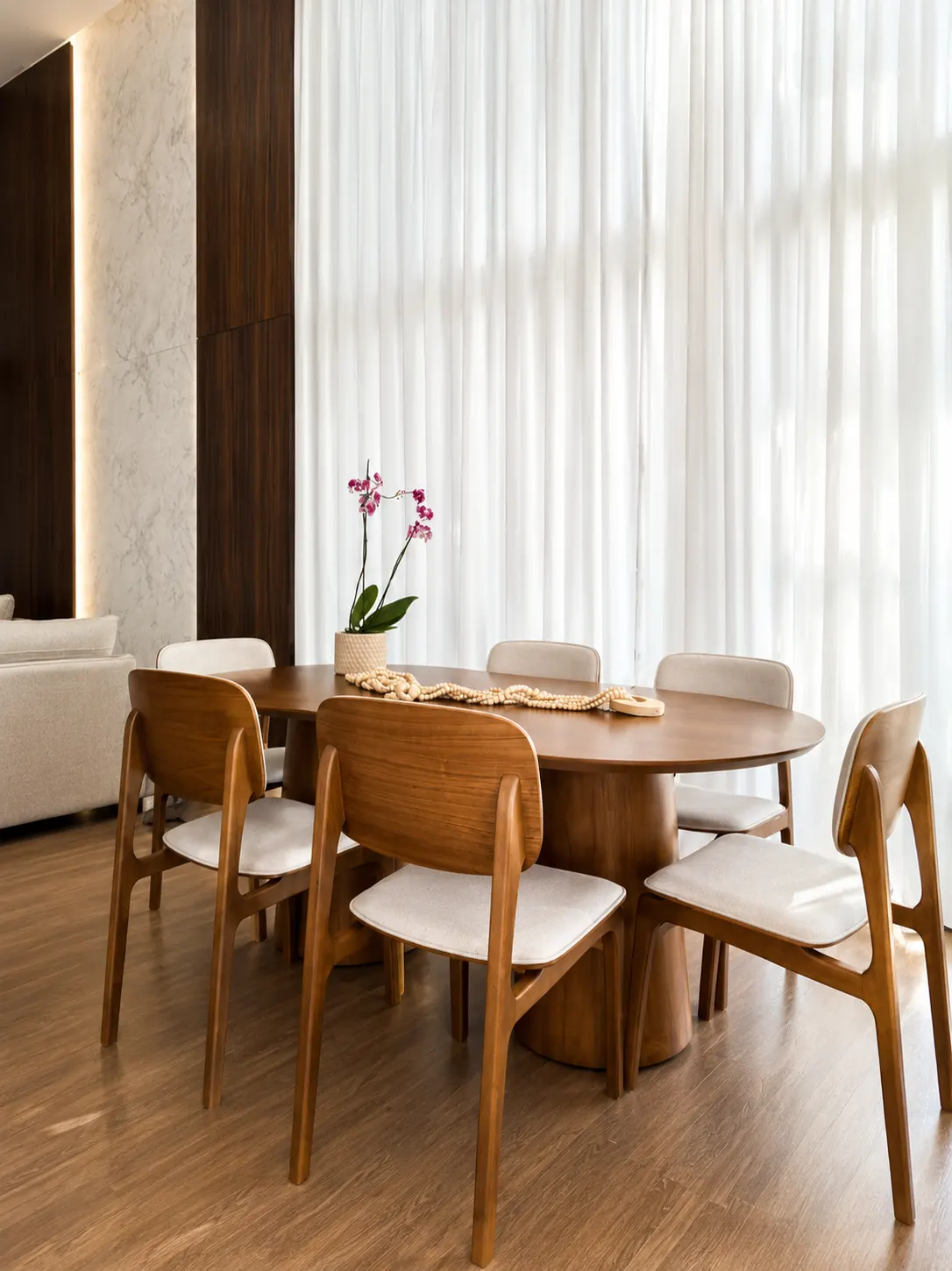 Mesa de jantar oval em madeira com cadeiras de design e orquídea ao centro
