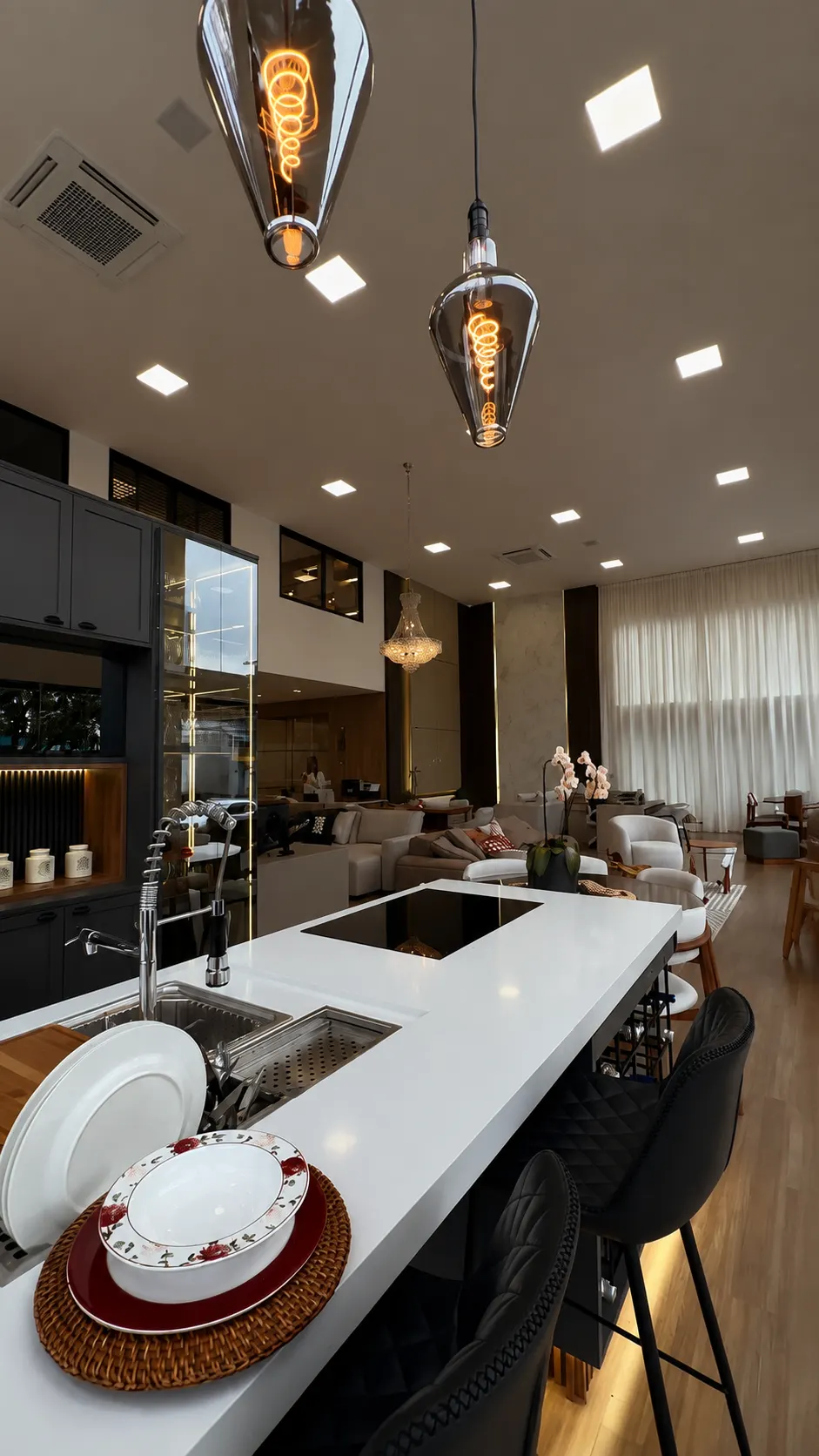 Cozinha planejada com ilha em quartzo branco e pendentes de vidro fumê no showroom Real Design